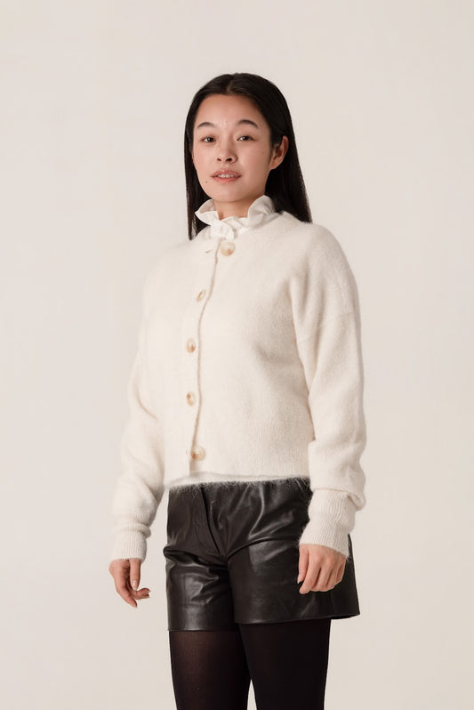 Person wearing a white wool and alpaca cardigan over black leather shorts