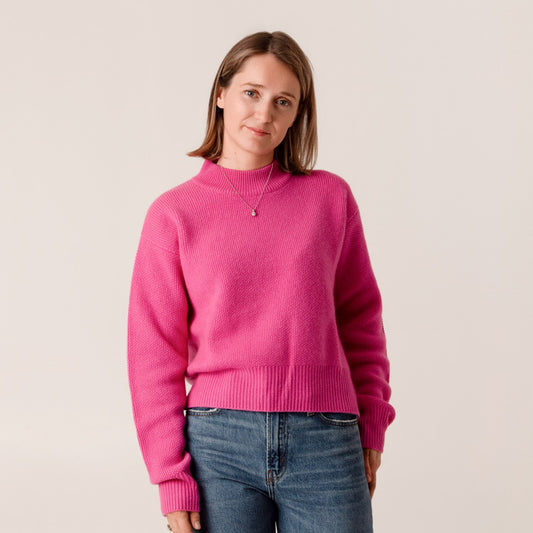 Person wearing a bright pink wool and cashmere sweater and blue jeans