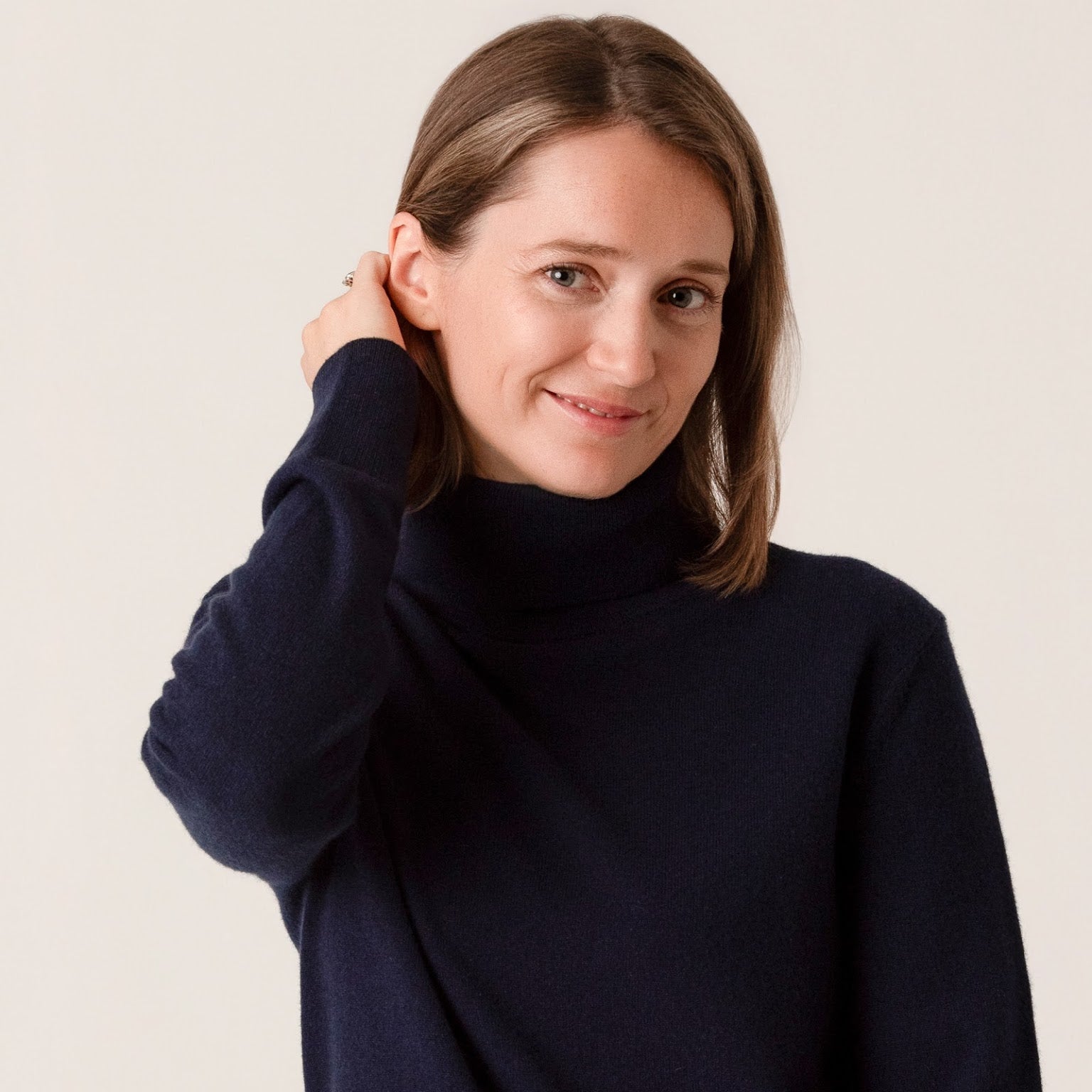 Woman wearing a navy blue turtleneck sweater against a plain background