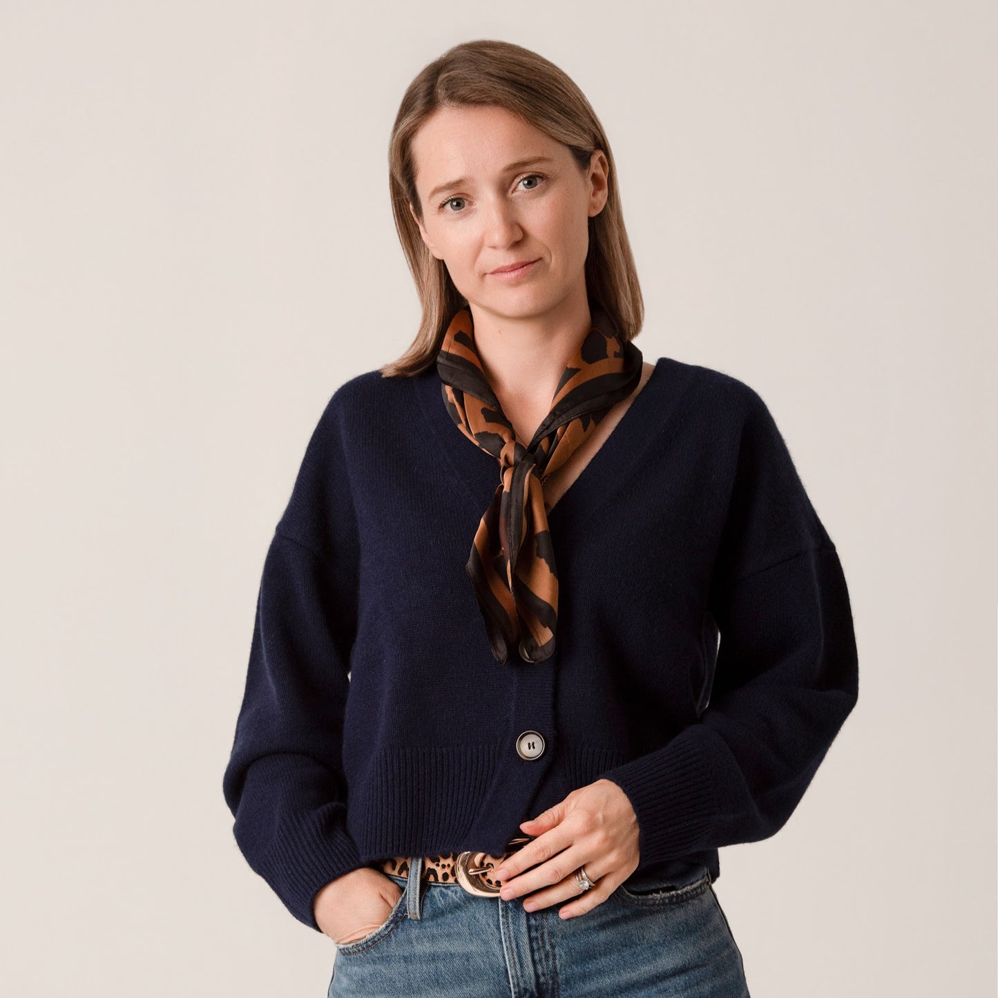 Woman wearing a navy sweater and patterned scarf against a plain background