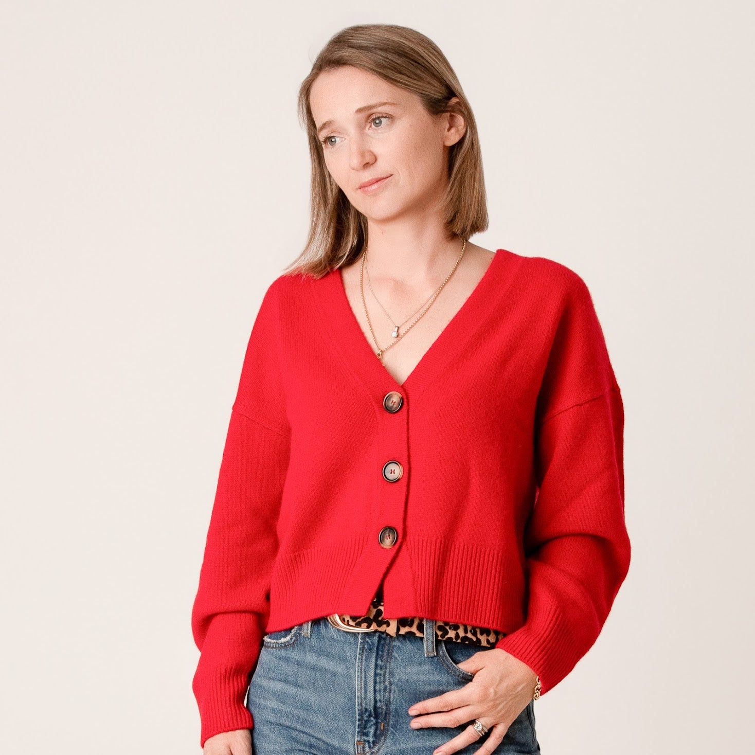 Woman wearing a red  wool and cashmere cardigan with blue jeans on a beige background