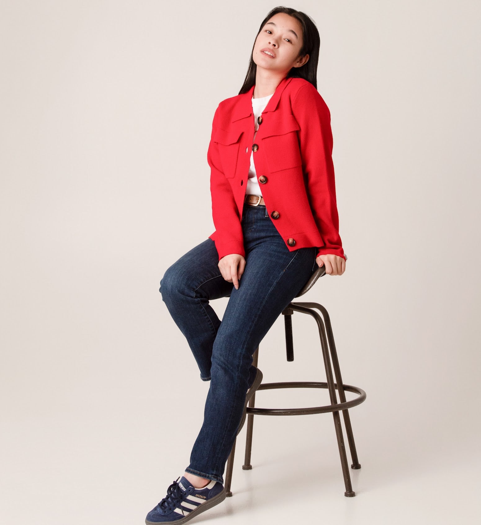 Person wearing a red wool jacket  with blue jeans sitting on a stool 