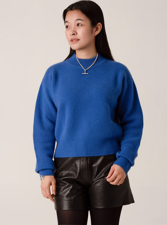 Person wearing a blue cashmere and wool sweater with black leather shorts and silver jewellery